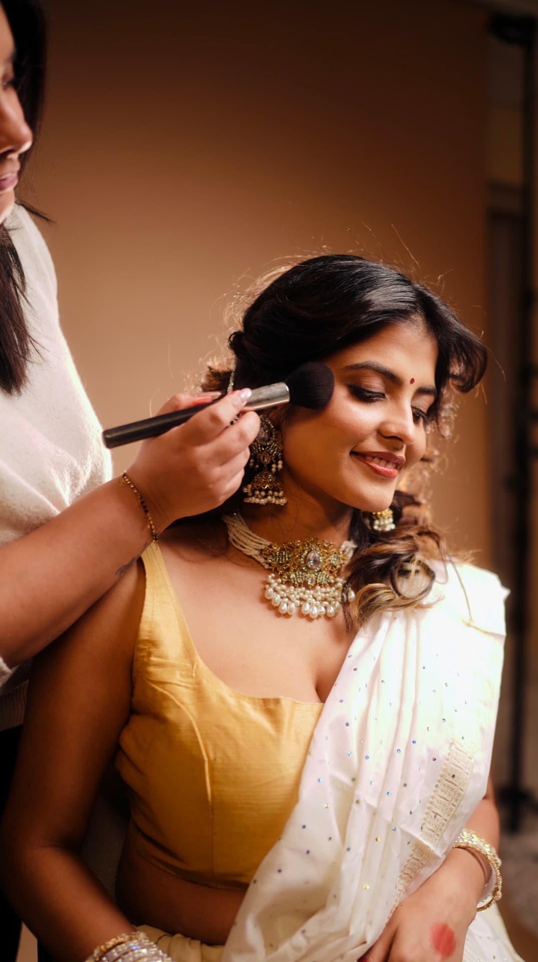 South Asian bride with crystal headpiece peering over embellished pink veil