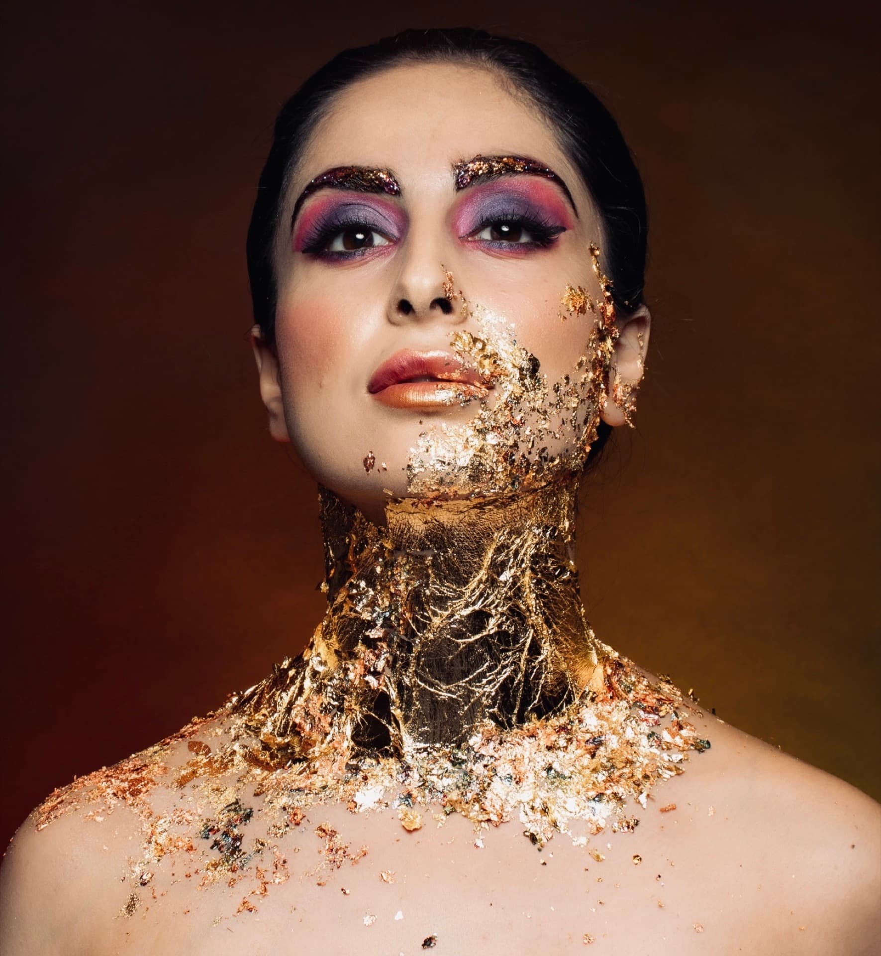 Avant-garde beauty editorial with gold leaf face art and purple eyeshadow